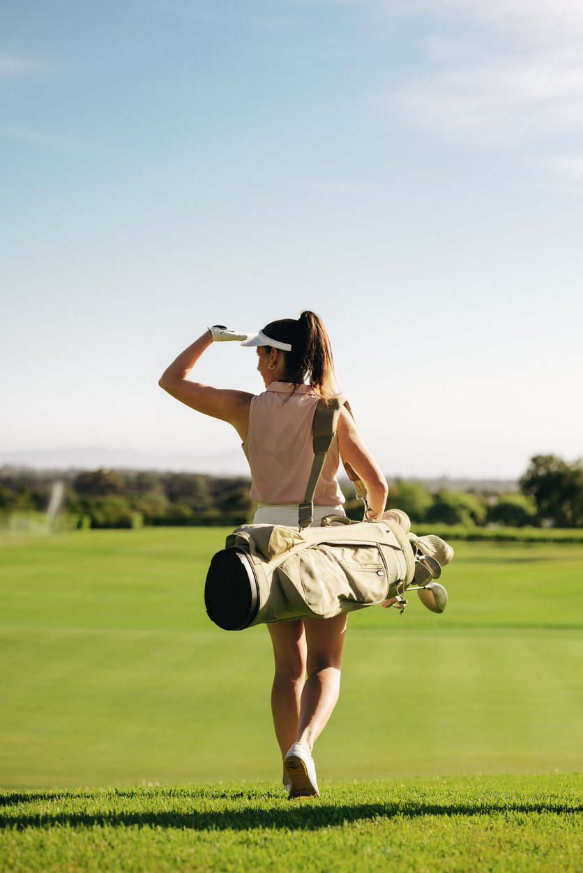Professional female golfer carries golf gear on the fairway at a golf resort on a bright and sunny morning